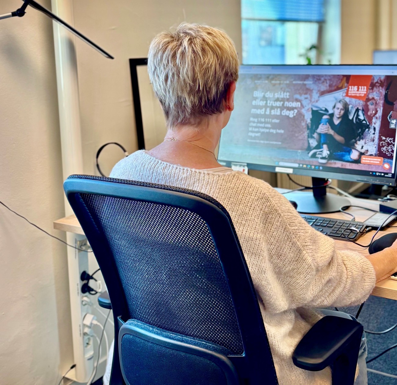 Dame på Alarmtelefonen som sitter ved arbeidsstasjonen. 